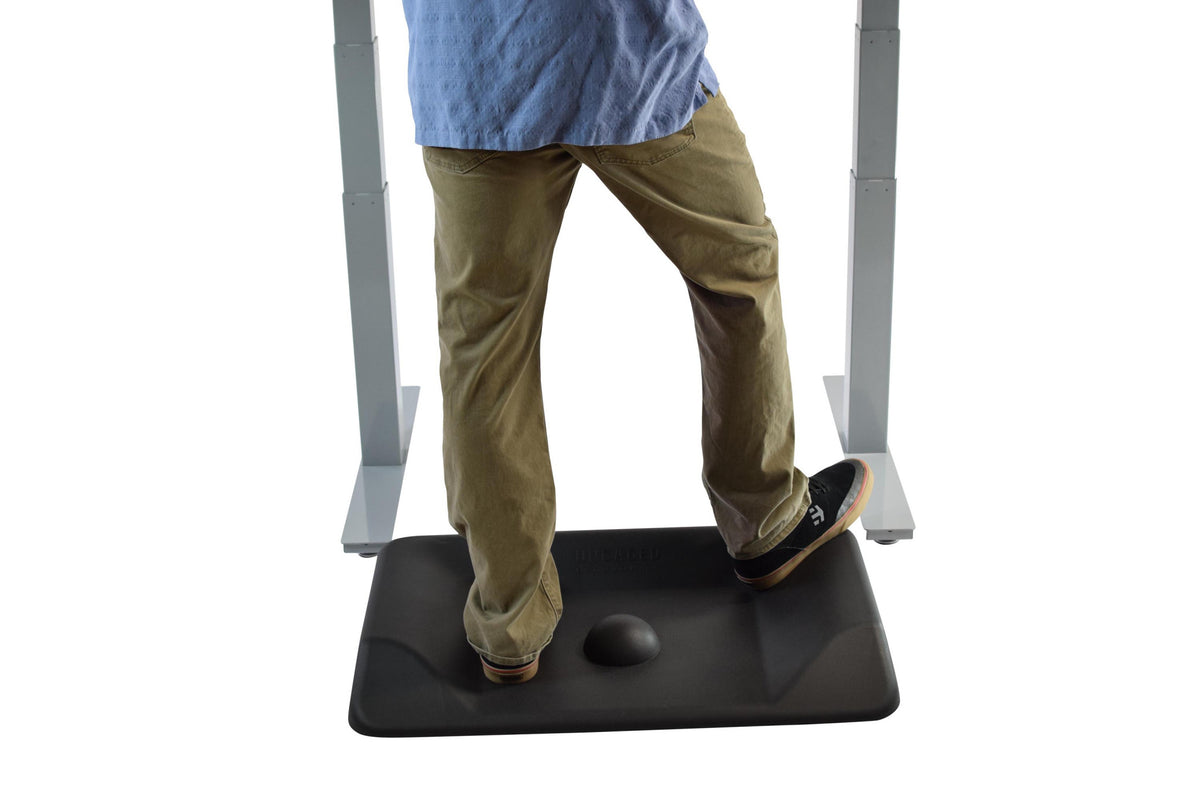 Man stepping off black anti-fatigue mat at standing desk showing center massage ball