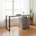Gray and black computer desk with 3 drawers by a bright window